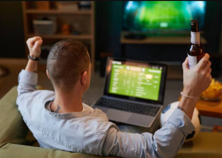 Bettor drinks beer and enjoys games while betting online on laptop